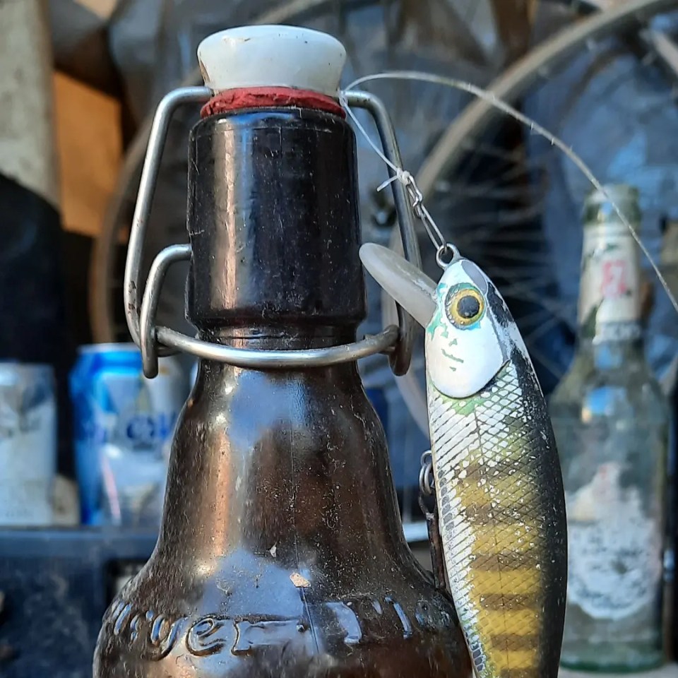 Bierflasche und Angelköder im Vordergrund, Müll im Hintergrund